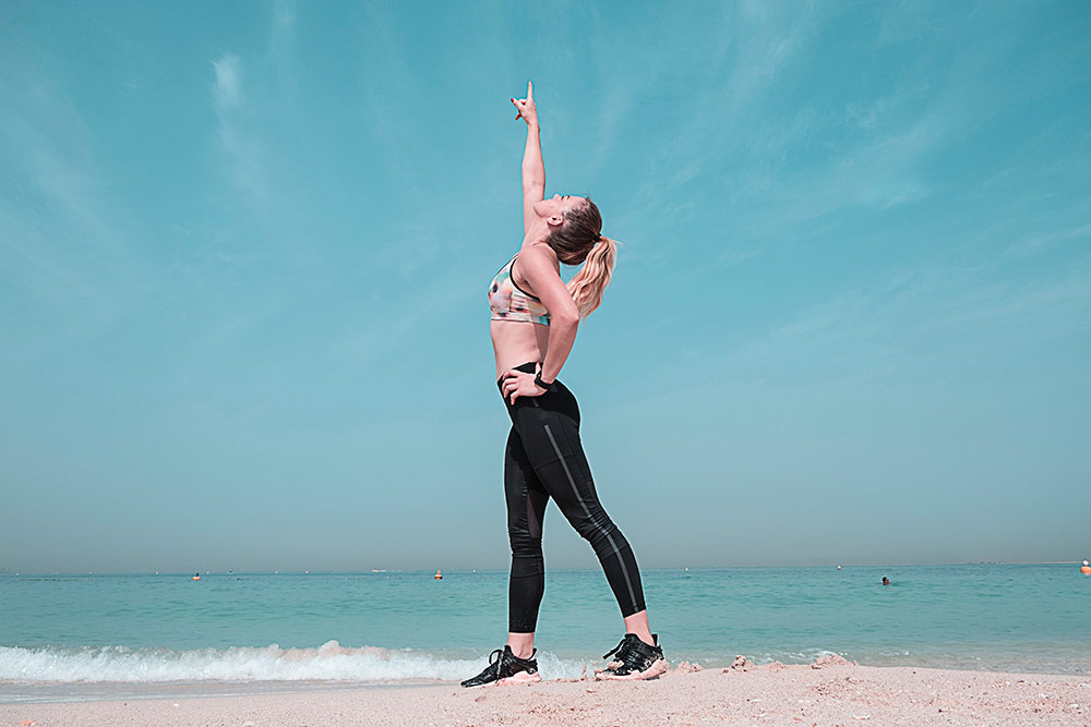 Woman standing on the beach in athletic gear pointing at the sky