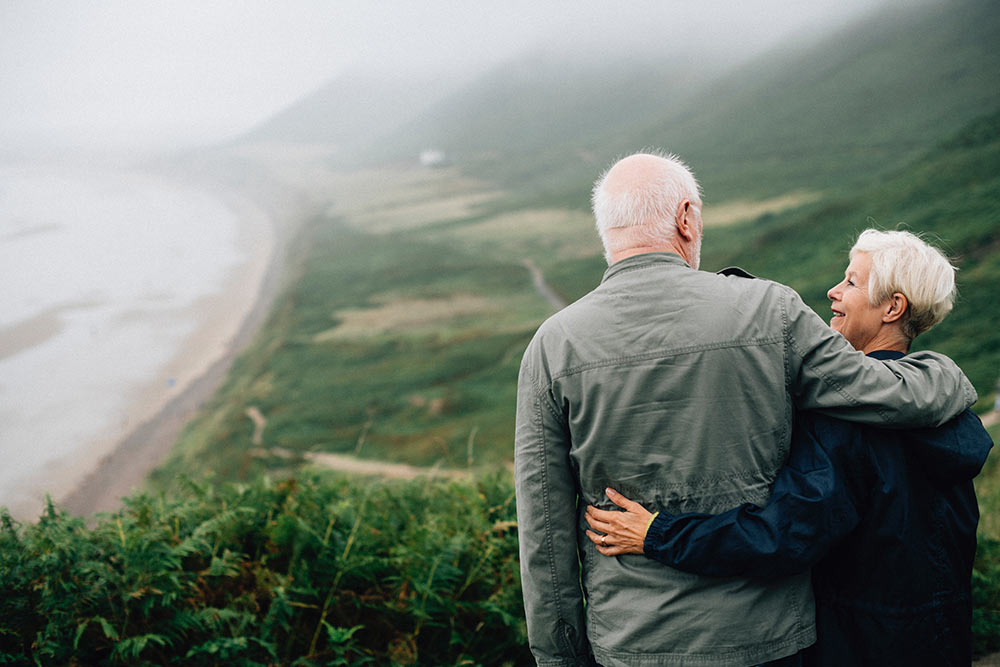 Older couple standing on a hill looking over a shore and water