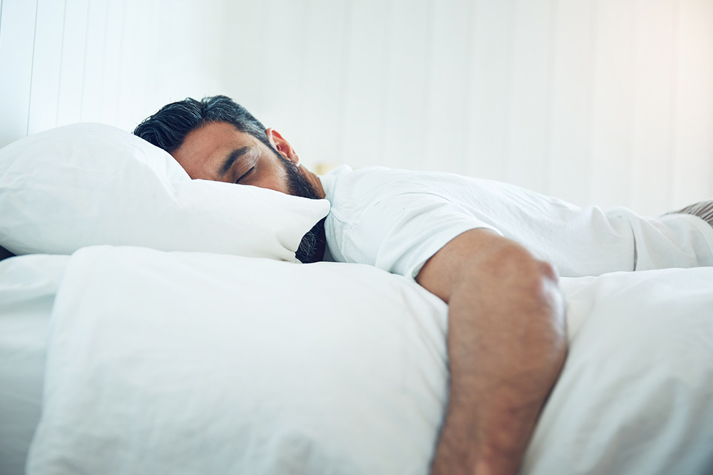 man asleep on a bed with white sheets