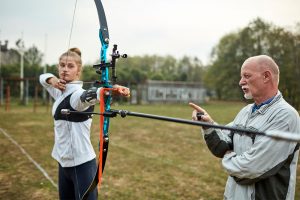 Male coach coaching female archery athlete